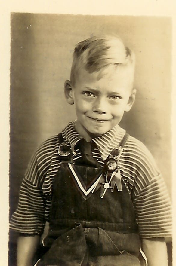 Sepia portrait of a smiling young blond boy in a striped shirt and overalls.