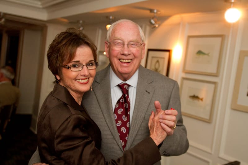 Don in a gray jacket and paisley tie, dancing and smiling with Eileen, who wears glasses and a brown jacket.