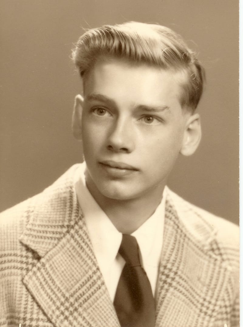 Sepia portrait of a teenage boy with swept-back hair, wearing a plaid jacket and a dark tie.